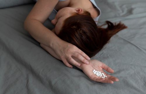 Девушка лежит с таблетками в руке